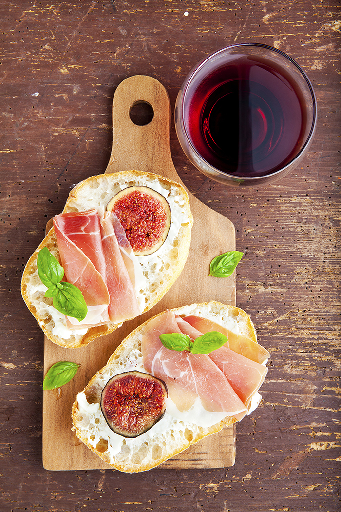bruschetta with prosciutto ham & figs with white cheese. fresh basil. red wine in the glass. italian appetizer.