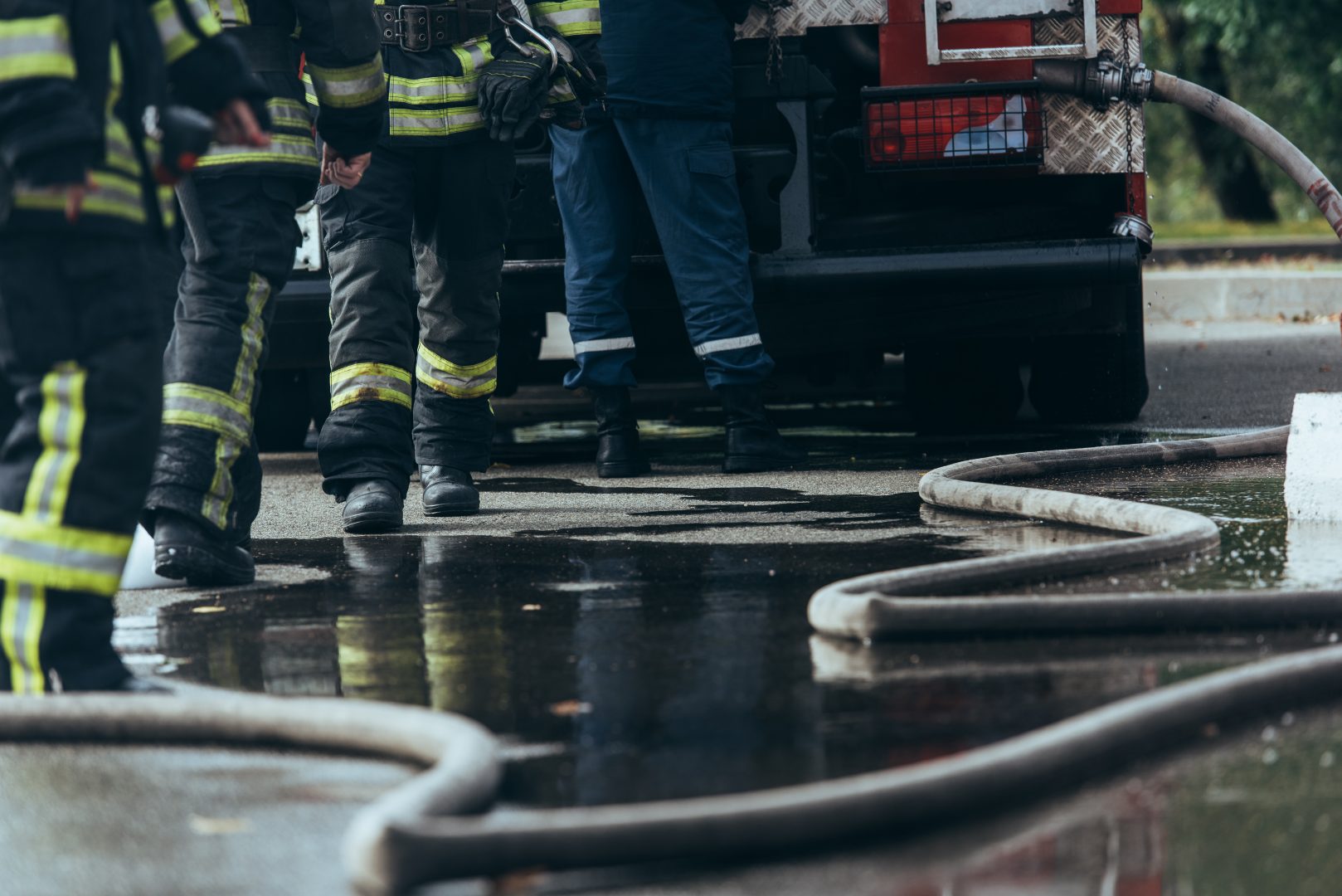 Firefighters in protective gear standing near a fire truck with water hoses on a wet pavement.