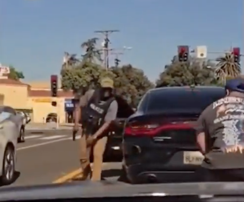 An ICE officer draws his gun as he confronts a man behind the officer's vehicle in the middle of a Pasadena street on June 18, 2025.