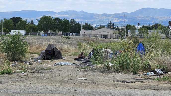 A county resident experiencing homelessness camps in a field near the 210 Freeway and Highland Avenue in San Bernardino.