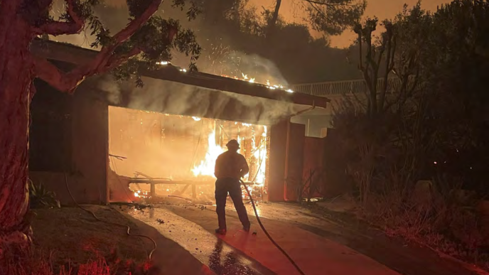 A firefighter battles flames that have engulfed a home during the LA wildfires in January.