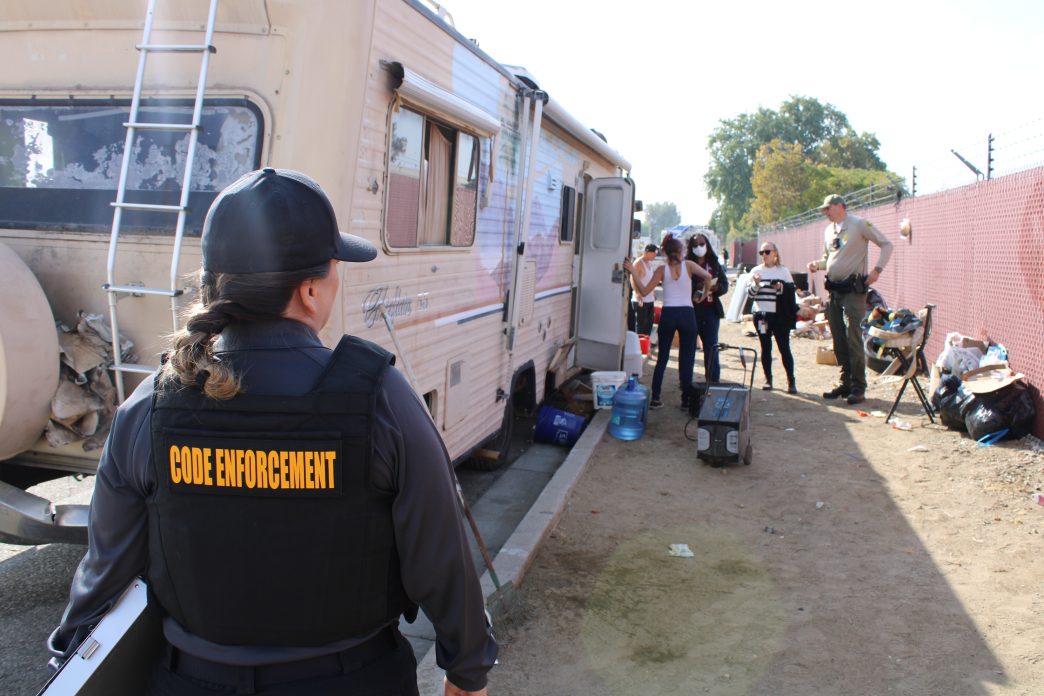 Code Enforcement officers, Office of Homeless Services workers and a sheriff's deputy meet county residents living in an encampment Wednesday in an unincorporated area near Fontana.