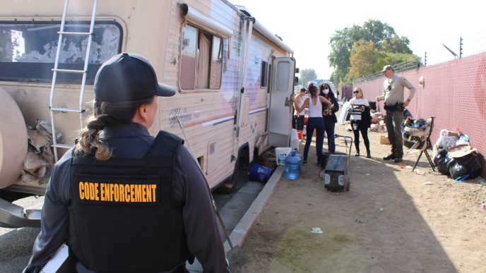 Code Enforcement officers, Office of Homeless Services workers and a sheriff's deputy meet county residents living in an encampment Wednesday in an unincorporated area near Fontana.