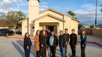 Housing Secretary Tomiquia Moss, fifth from right, stands with county Supervisor Jesse Armendarez, fourth from right, along with county leaders and housing partners gather in front of the former chapel at Pacific Village, which is being converted into housing units.