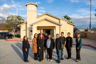 Housing Secretary Tomiquia Moss, fifth from right, stands with county Supervisor Jesse Armendarez, fourth from right, along with county leaders and housing partners gather in front of the former chapel at Pacific Village, which is being converted into housing units.