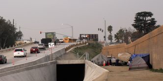 An encampment lines the sound wall near a local freeway.