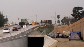 An encampment lines the sound wall near a local freeway.