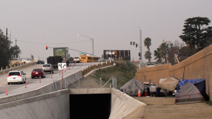 An encampment lines the sound wall near a local freeway.