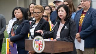 Community members led by LA County Supervisor Hilda Solis, at podium, along with Los Angeles Mayor Karen Bass and City Councilwoman Ysabel Jurado, front row, call for Lineage Logistics to pay for recovery efforts following a large warehouse fire in Boyle Heights.