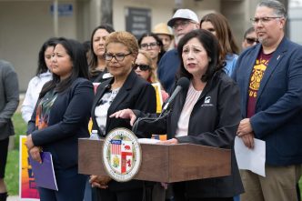 Community members led by LA County Supervisor Hilda Solis, at podium, along with Los Angeles Mayor Karen Bass and City Councilwoman Ysabel Jurado, front row, call for Lineage Logistics to pay for recovery efforts following a large warehouse fire in Boyle Heights.