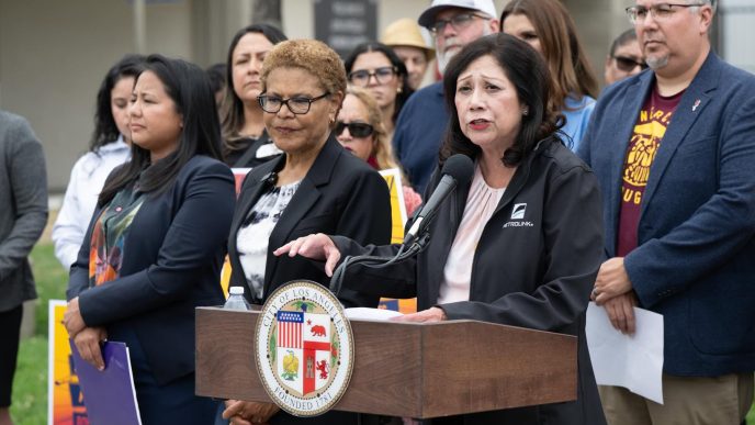 Community members led by LA County Supervisor Hilda Solis, at podium, along with Los Angeles Mayor Karen Bass and City Councilwoman Ysabel Jurado, front row, call for Lineage Logistics to pay for recovery efforts following a large warehouse fire in Boyle Heights.
