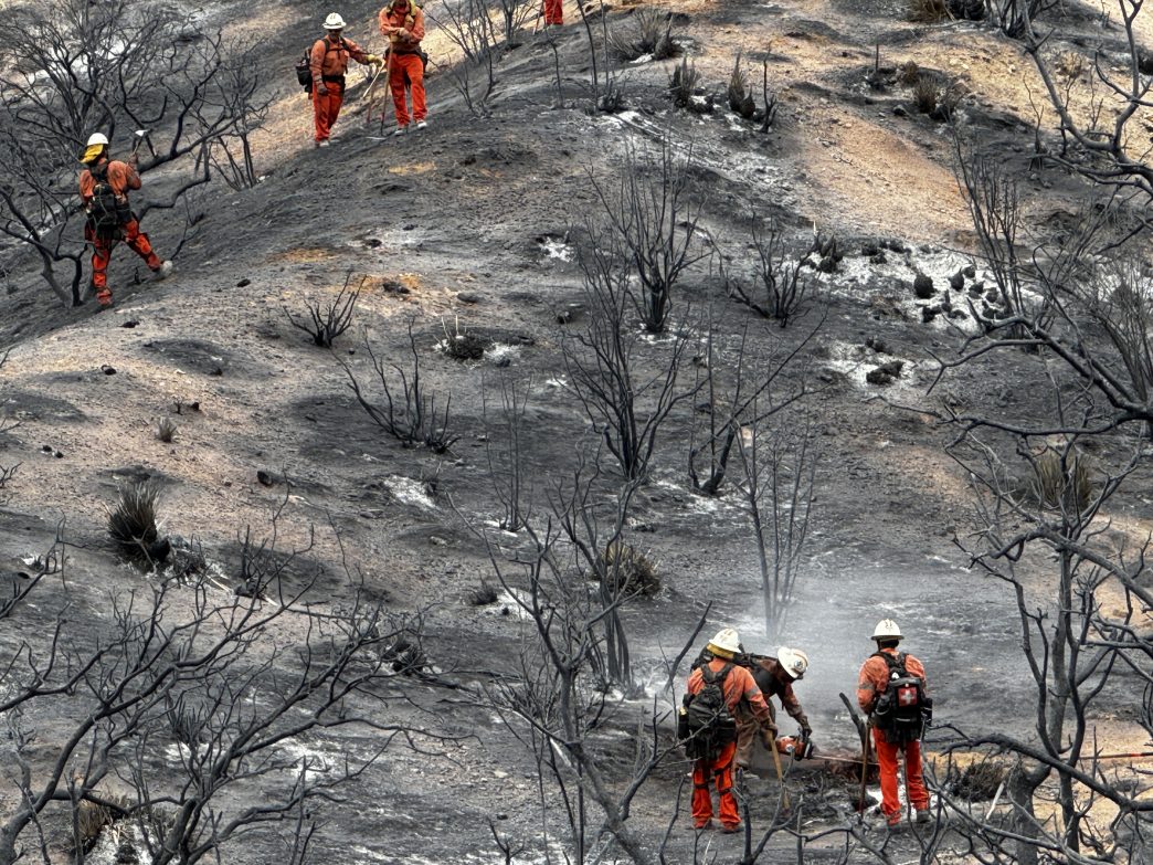 Firefighters traverse a smoldering hill near Llano.
