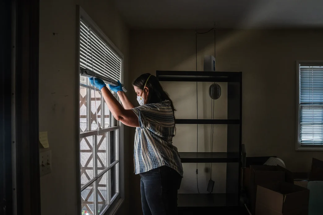 Gil Barel moves the blinds up to let in more light into her living room in Pasadena on Aug. 2, 2026. Barel is currently not living in her apartment because of the Eaton Fire of January 2025.