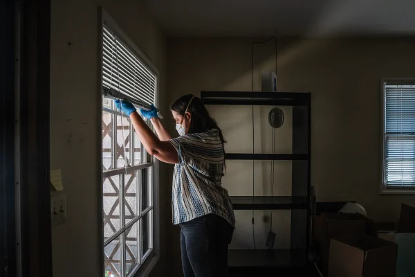 Gil Barel moves the blinds up to let in more light into her living room in Pasadena on Aug. 2, 2026. Barel is currently not living in her apartment because of the Eaton Fire of January 2025.