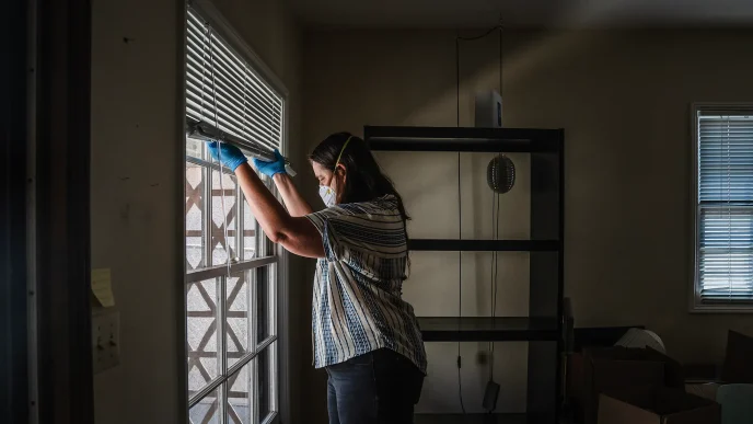 Gil Barel moves the blinds up to let in more light into her living room in Pasadena on Aug. 2, 2026. Barel is currently not living in her apartment because of the Eaton Fire of January 2025.