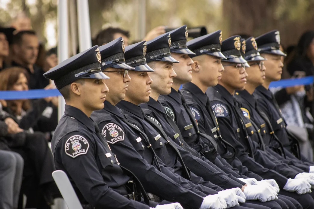 A row of Los Angeles School Police officers in uniform sit together during an outdoor ceremony.