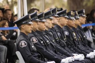 A row of Los Angeles School Police officers in uniform sit together during an outdoor ceremony.